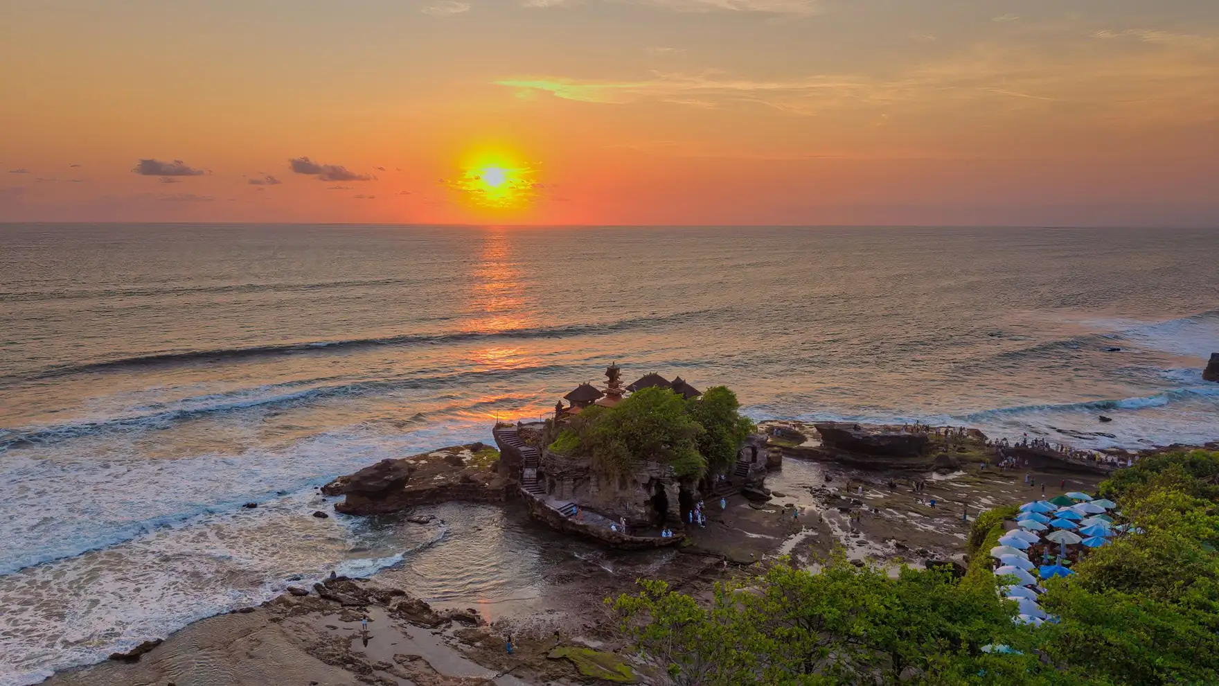 A breathtaking sunset over the iconic Tanah Lot Temple in Bali, Indonesia, casting vibrant reflections on the ocean