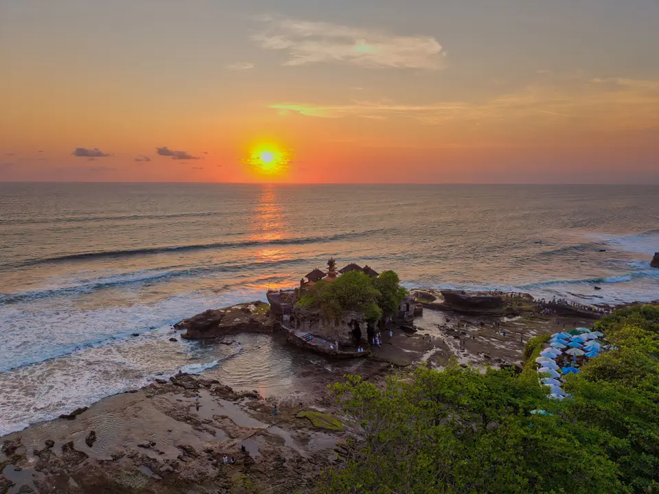 A breathtaking sunset over the iconic Tanah Lot Temple in Bali, Indonesia, casting vibrant reflections on the ocean