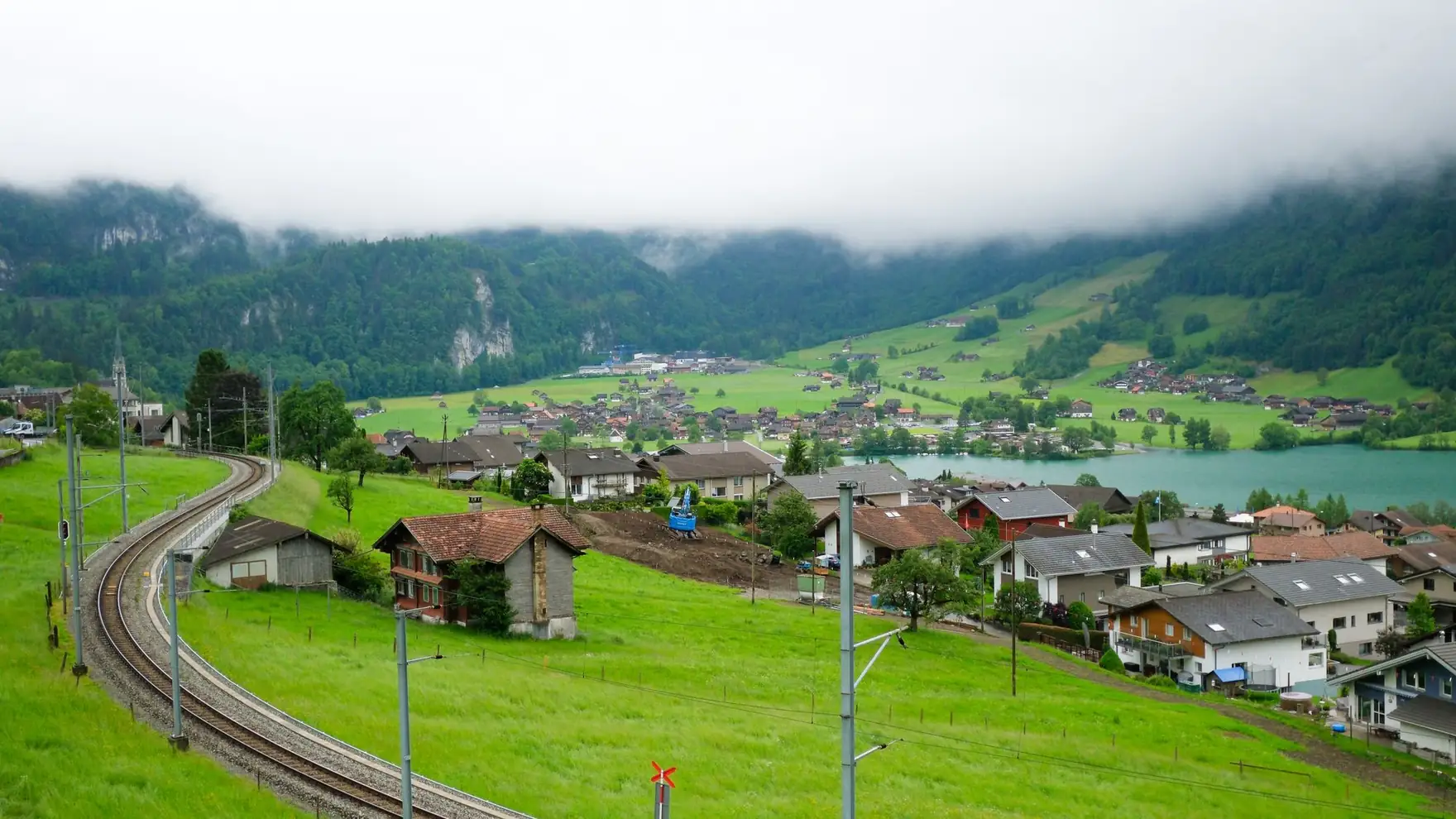 Beautiful shot of Lungern village in Switzerland with lush green hills and railway. Misty mountains in the backdrop