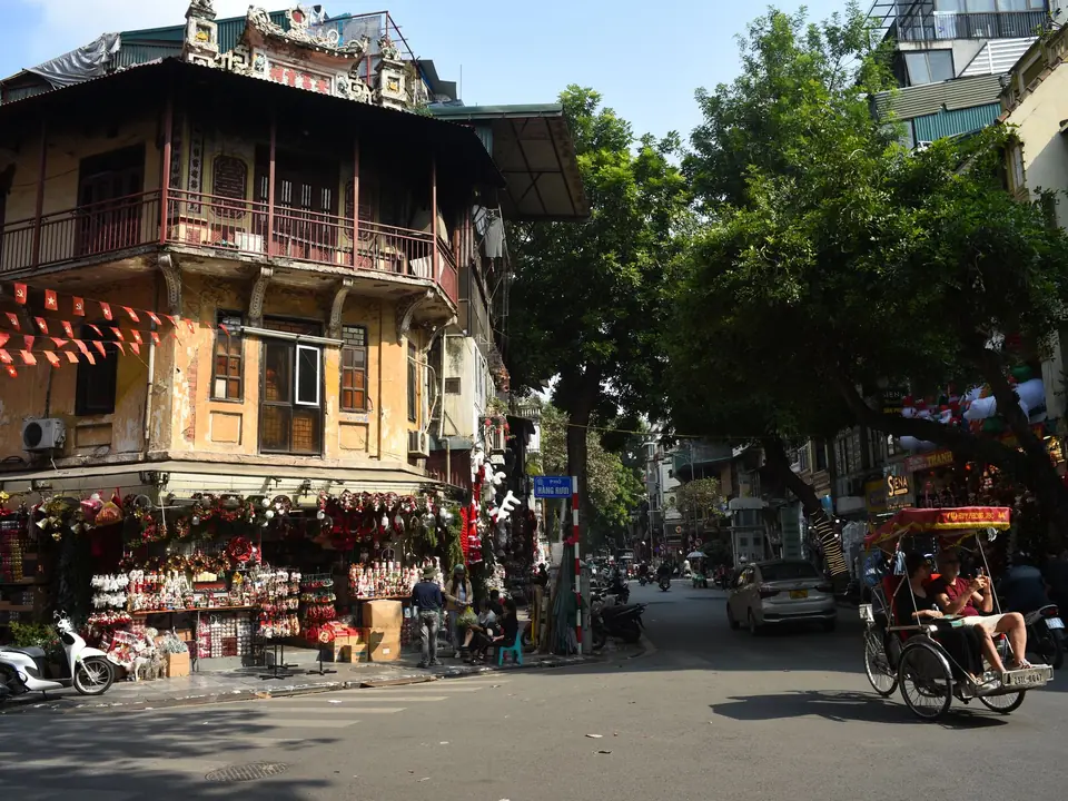 Lively street corner in Hanoi featuring traditional architecture and a passing rickshaw