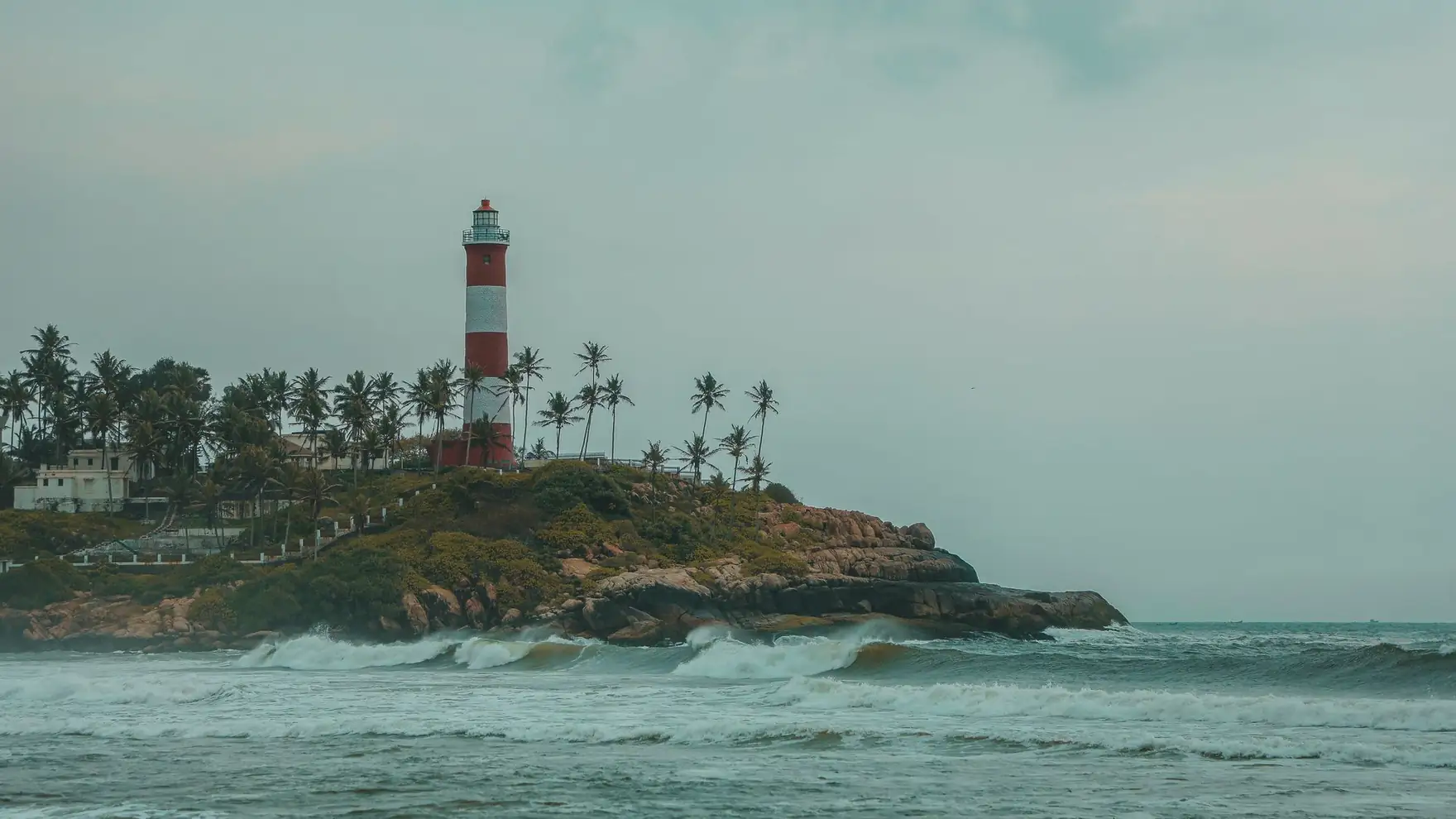 Scenic view of Kovalam Beach lighthouse with palm trees and rocky shore in Kerala, India