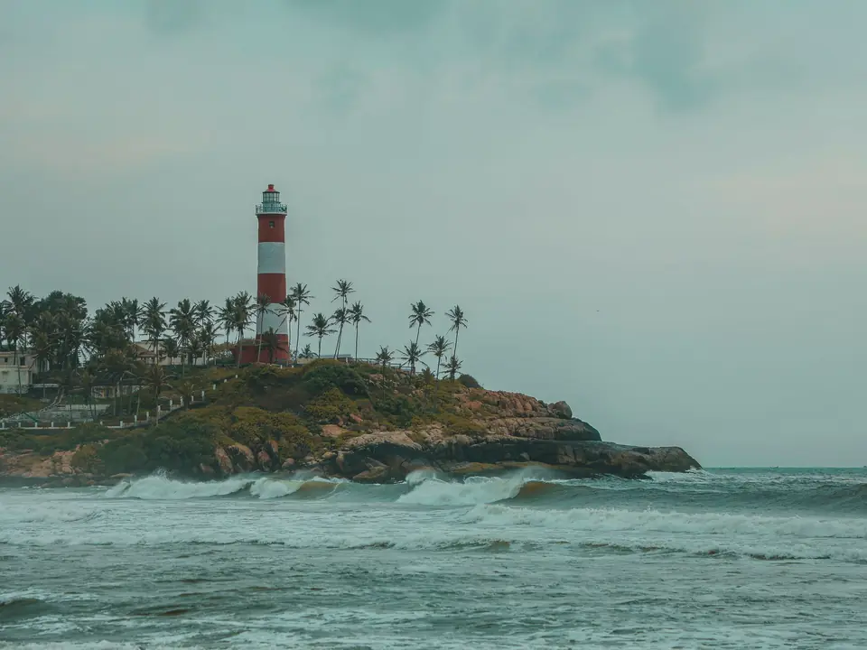 Scenic view of Kovalam Beach lighthouse with palm trees and rocky shore in Kerala, India