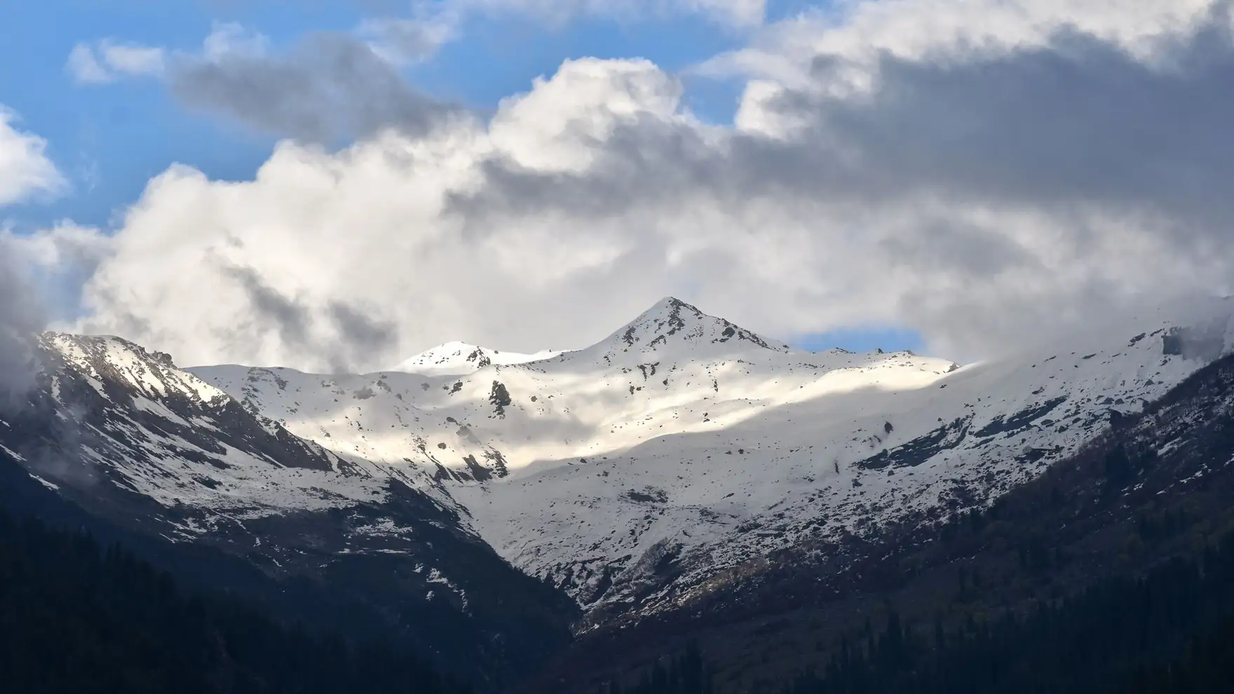 Stunning view of snow-covered mountains in Manali, HP, India under dramatic clouds and blue sky