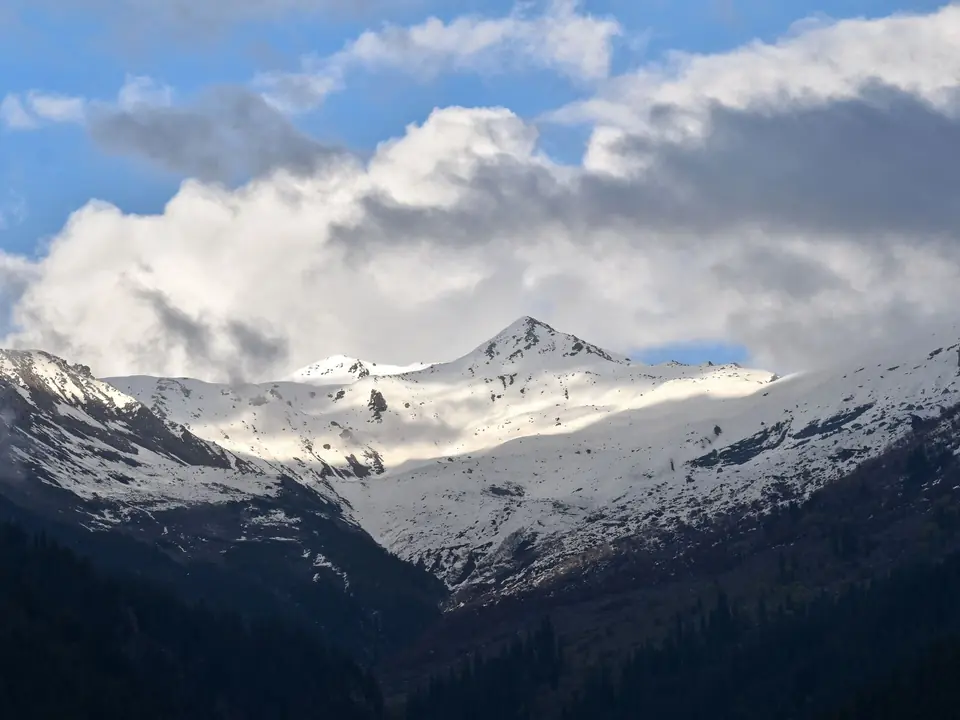 Stunning view of snow-covered mountains in Manali, HP, India under dramatic clouds and blue sky